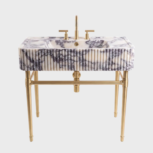A modern bathroom vanity featuring a rectangular white marble sink with dark gray veining, supported by a gold-finished metal frame with fluted detailing and a matching gold faucet.