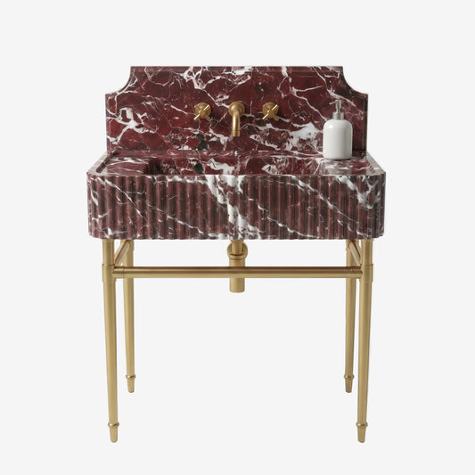 A vintage-style bathroom vanity featuring a deep rectangular basin and matching backplate in red and white marble, supported by a polished gold brass stand with elegant legs. The vanity is equipped with a central gold faucet and two separate gold wall-mounted faucets, and a small white soap dispenser sits on the right side.