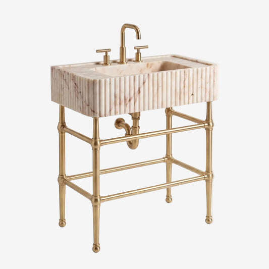 A freestanding bathroom vanity with a rectangular marble sink featuring vertical fluting, a curved brass faucet, and a matching brass double-handle faucet and support frame, shown on a light gray studio background.