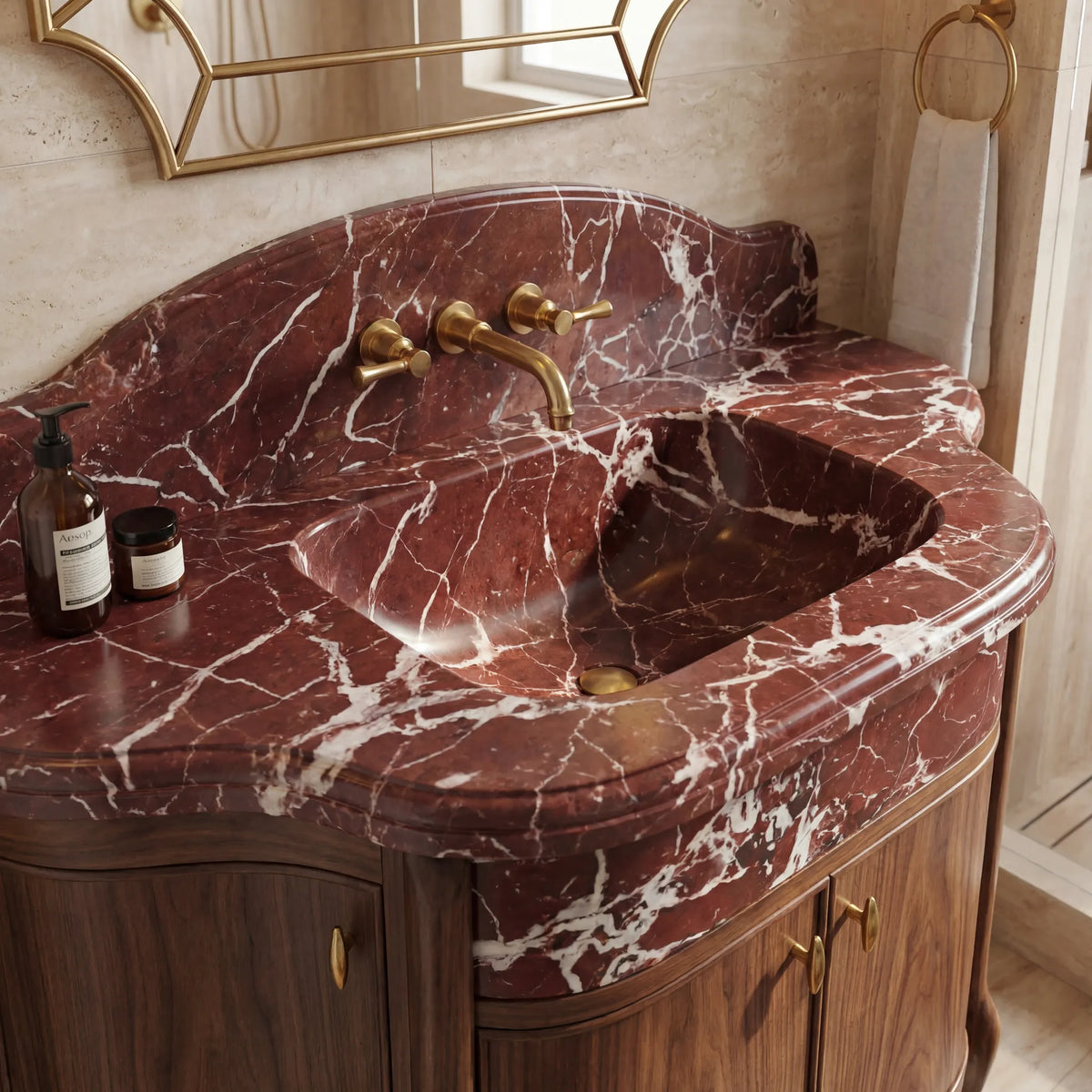 Close-up of Rosso Levanto marble bathroom sink with scalloped backsplash and brass wall-mounted faucet